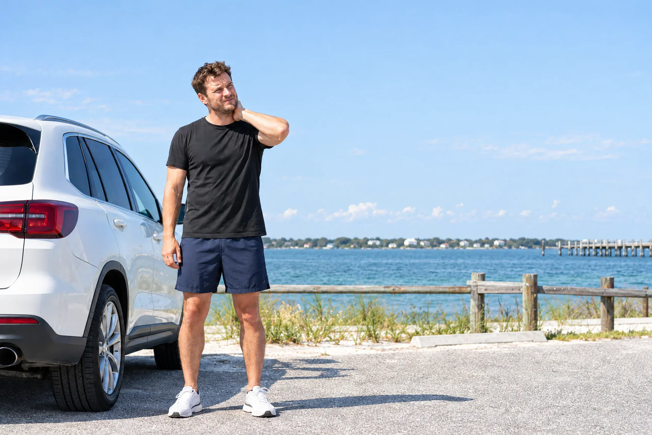 Adult rubbing a stiff neck beside a parked car days after an accident, seeking pain care near Navarre, FL